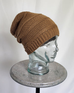 A three quarter view of a Kinsol Trestle Toque the colour of brown sugar, displayed on a glass head.  The had is snug around the head, with a bit of slouch in the back.
