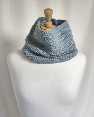 A head-on view of the Foggy Morning Cowl by Tanis McNally-Dawes, modeled on a white cloth mannequin.  The cowl is a steel blue and sits proud on the mannequin's shoulders.